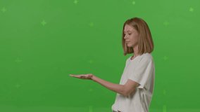 Young caucasian woman rotating something invisible on her hand , showing a product, smiling and cheerful, offering an imaginary object on a Green Screen, Chroma Key background. 4k UHD footage video