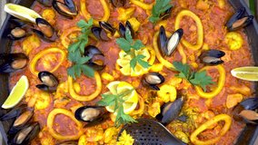Homemade Paella. Traditional Spanish food made with rice, 
seafood, shrimps, vegetables, mussels, squid, tomatoes, saffron. Glass of Sangria on right cornet. Camera zoom out. Stabilized video