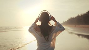 Relax asian woman wearing headphones walking in the sea beach at golden sunset - Female tourist listening to music on summer vacation - Powered by Shutterstock - Get 15% off with code: PIKWIZARD15