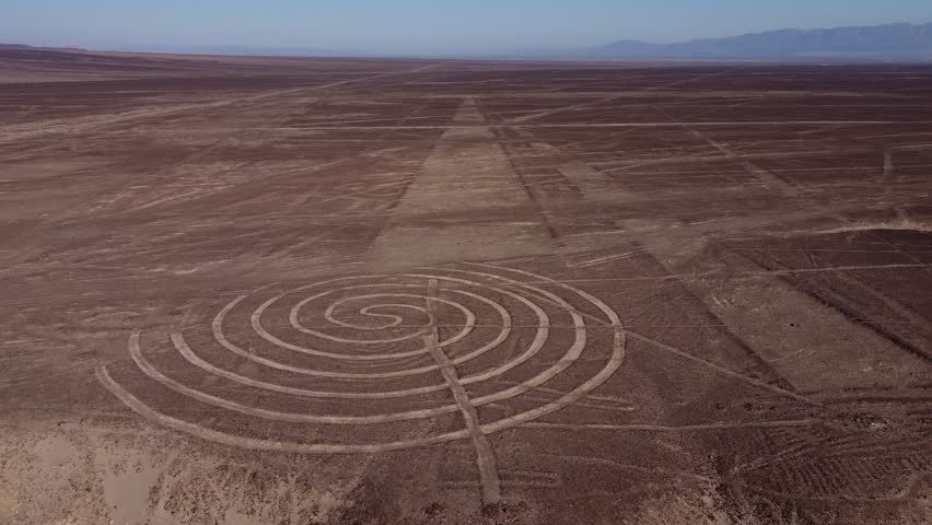 Aerial 4k video of the Nazca Lines. Drone flies backwards from a spiral ancient geoglyph. Desert plateau also filled with many long lines. Located in Nazca, Peru. Royalty-Free Stock Footage #1104689317