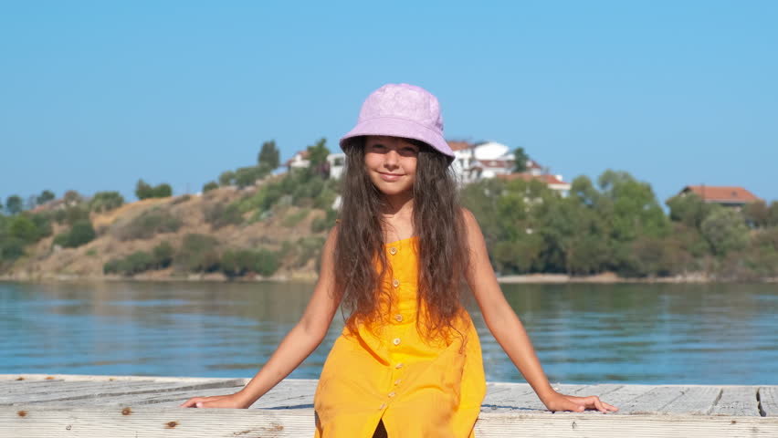 Happy rest on sea platform. A smiling child raise her arms and sit on the sunny platform on the tropical gliff.