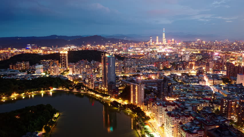 Night skyline of downtown Taipei at dusk, the capital city of Taiwan, with 101 Tower standing amid skyscrapers in XinYi District and residential buildings by Bihu Park in Neihu under blue twilight sky Royalty-Free Stock Footage #1104695179