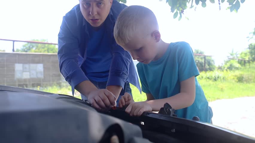 Oil level check. A man shows his son how to check the oil level in a car engine. The father teaches the kid how to work the systems of the internal combustion engine.  Royalty-Free Stock Footage #1104702557