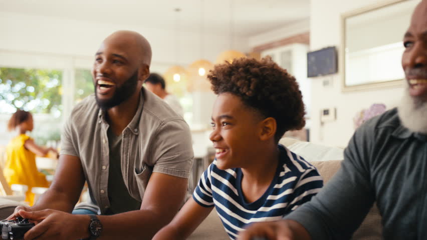 Close up of multi-generation male family sitting on sofa at home holding controllers playing video game together - shot in slow motion | Shutterstock HD Video #1104705475