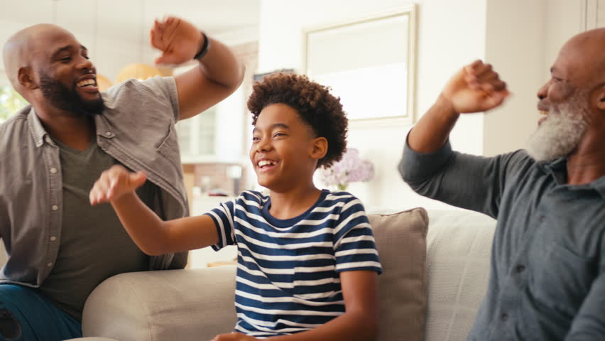 Multi-generation male family sitting on sofa at home holding controllers playing video game together giving each other high five - shot in slow motion | Shutterstock HD Video #1104705497