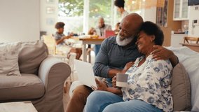 Senior couple at home looking at laptop together with multi-generation family in background - shot in slow motion - Powered by Shutterstock - Get 15% off with code: PIKWIZARD15