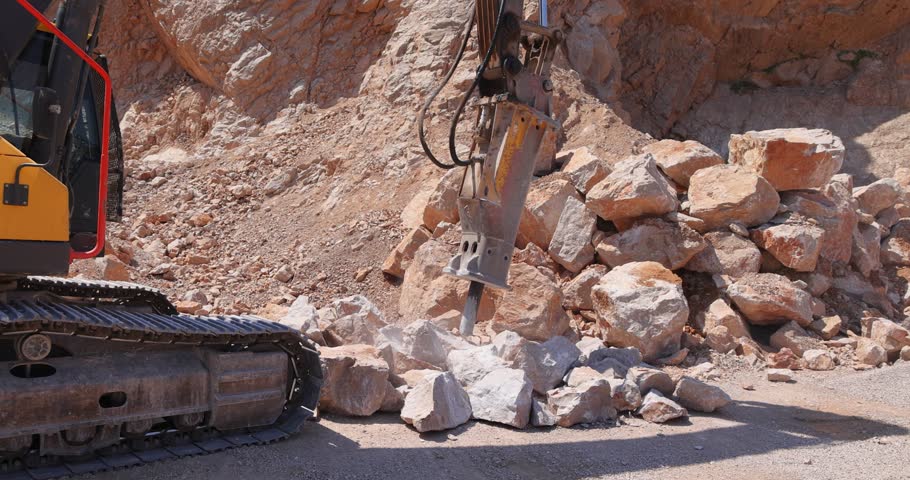 Excavator with hydraulic hammer breaking rock. Stone crushing machine at open pit mining and processing plant for crushed stone. Concepts of industry and building materials, slow motion Royalty-Free Stock Footage #1104708287