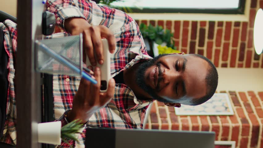 Happy excited competitive gamer playing engaging videogames on smartphone, enjoying himself. Cheerful man having fun on phone in relaxed stylish warm apartment living room