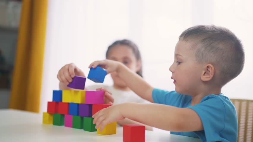 children in kindergarten play with blocks on table by the window. education development children game concept. children play with blocks at home rejoice having. children play together at fun home Royalty-Free Stock Footage #1104712009