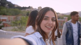 POV selfie of smiling young European girl looking camera shooting video for social media at rooftop party with friends. Groups of persons dancing and drink wine glasses. Relationships in youth people
