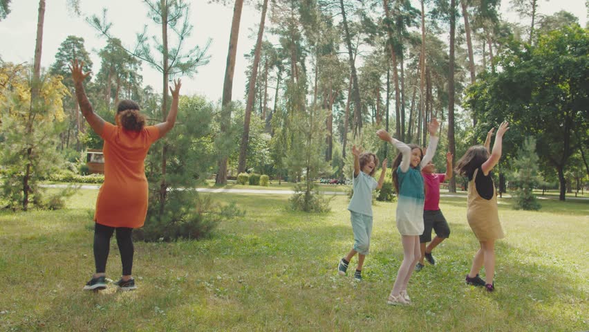 Charming group of diverse kids dancing, laughing, having fun led by cheerful young woman during outdoor classes. Smiling children enjoying school pastime in public park Royalty-Free Stock Footage #1104715123