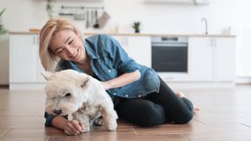 Loyal West Highland White Terrier staying in adult woman's embraces while being inside modern apartment. Loving pet owner kissing her furry best friend while enjoying daily interaction with dog. - Powered by Shutterstock - Get 15% off with code: PIKWIZARD15
