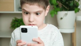 A 5-year-old boy watches cartoons on his smartphone, looks at the screen and rubs his tired eyes.