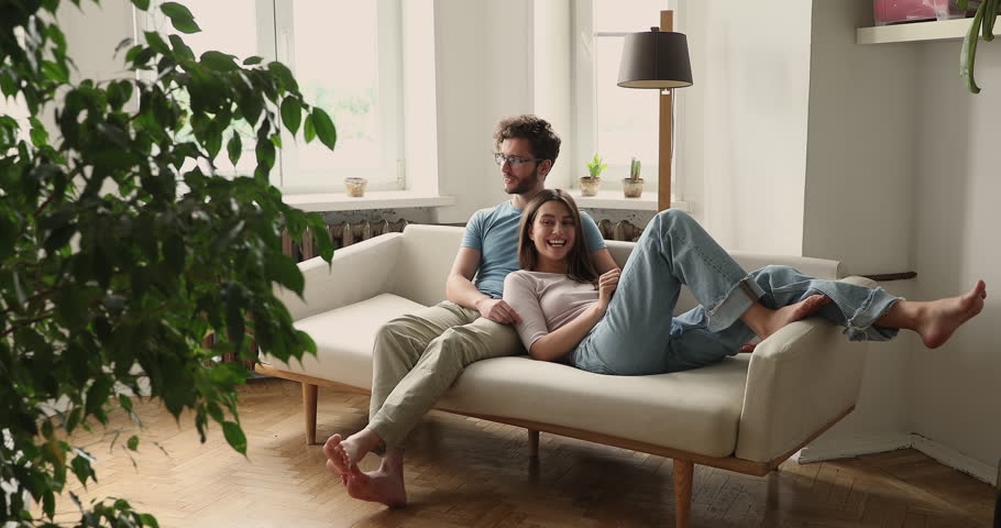 Peaceful serene young couple cuddle on soft cozy sofa at home talk chat smile share plans ideas on future. Affectionate millennial husband sit on couch embrace beloved wife enjoy pleasant conversation Royalty-Free Stock Footage #1104723481