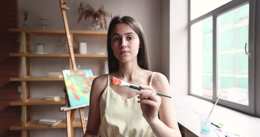 Artist woman standing in art studio workshop hold paintbrush painting over camera glass, applying bright red paints like on canvas, make hand movement with brush along screen, close up. Creative hobby Royalty-Free Stock Footage #1104723493