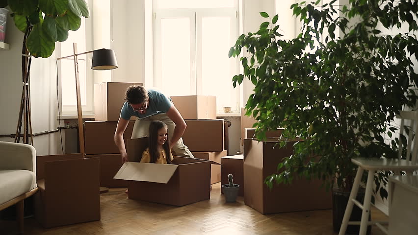 Delivery service. Joyful young dad play with daughter push little girl sitting in box around living room at moving day. Happy kid having fun with father enjoy riding in cardboard package by new flat Royalty-Free Stock Footage #1104723501