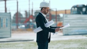 Video of elegant architect in helmet looking at blueprints while checking construction