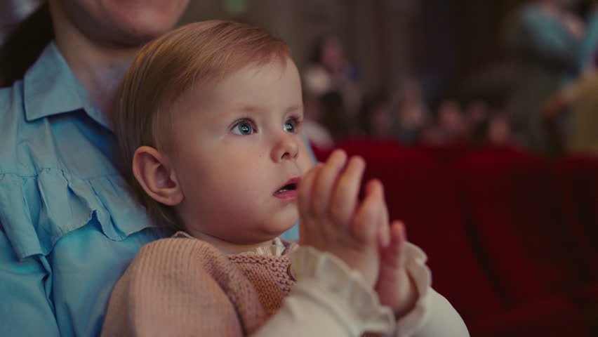 Happy baby girl having fun and clapping with admiration. Little child applauds looking at a performance in the theatre, a musical concert or a performance in a circus. Cultural event for children. Royalty-Free Stock Footage #1104726913