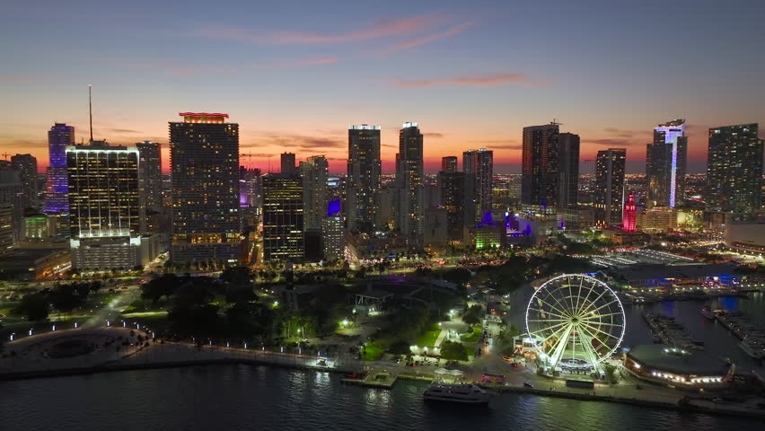 Skyviews Miami Observation Wheel at Bayside Marketplace with reflections in Biscayne Bay water and US urban landscape at night. High illuminated skyscrapers of Brickell, city's financial center