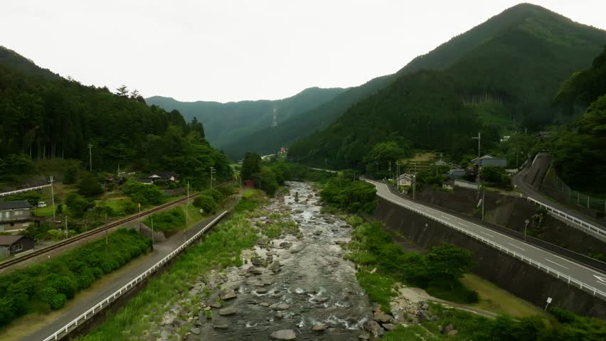 Red single-car train on track by river in green mountain landscape