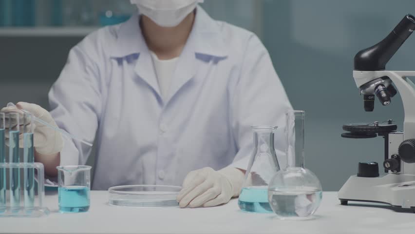 Biochemistry laboratory research, the scientist is doing an experiment - dropping the substance drop by drop into a petri dish. Lab glassware containing light blue liquid. Royalty-Free Stock Footage #1104733797