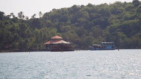 A video showing houseboats against an island full of trees during daytime in Thailand