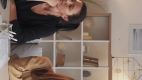 Vertical video. Family quarrel. Home conflict. Smiling mother teenage daughter making peace after argue hugging sitting desk light home interior.