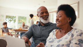 Senior couple at home looking at laptop together with multi-generation family in background - shot in slow motion - Powered by Shutterstock - Get 15% off with code: PIKWIZARD15