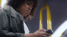 Low angle view of young afro woman traveling by underground and browsing a mobile phone. Shot with RED helium camera in 8K. 