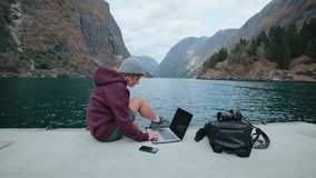 Social media content creator, young millennial photographer work remotely on laptop in epic Scandinavian scenery. Video blogger or influencer, travel around Norway and work on projects - Powered by Shutterstock - Get 15% off with code: PIKWIZARD15