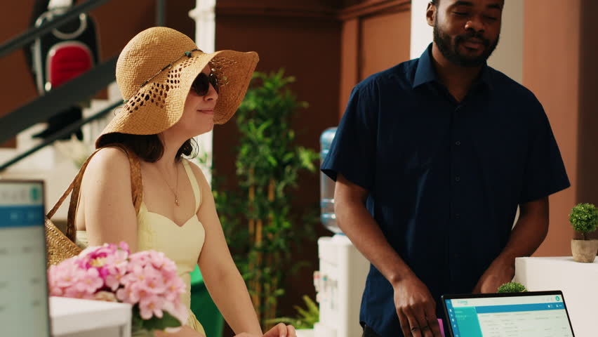 Tourists paying for room accommodation at resort, using credit card on pos terminal at front desk reception lobby. People on honeymoon vacation making payment upon their arrival. Handheld shot.