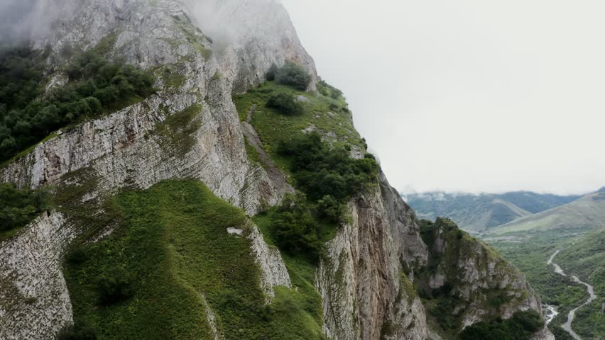 A rocky mountain slope overgrown with greenery, close-up. mountain valley with a river and fields in the lowland.