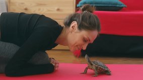 a young cute woman is basking with a red-eared turtle on a yoga mat. Female kisses a pet. The concept of human-animal friendship. High quality 4k footage. Cute funny video