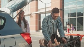 Young couple made food shoping. Guy is giving goods to girl. Two young people in love are loading car's truck with groceries. Couple bought lot paper bags full of vegetables and bread. - Powered by Shutterstock - Get 15% off with code: PIKWIZARD15