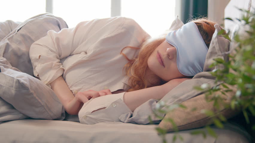 Caucasian girl with blindfold in bed in morning woman sleeping napping during daytime sleepy female waking up lying in comfortable bedroom peeks out from under sleep mask open eye fall asleep again Royalty-Free Stock Footage #1104758531