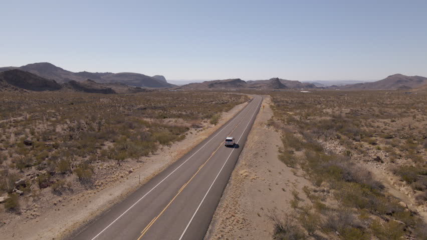 Aerial Shot Following Car on Highway Through Desert in Big Bend National Park in Texas, USA. Drone Shot of van driving in the middle of a desert highway in Big Bend