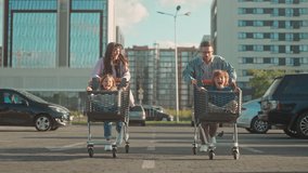 Family plays racing in parking lot. Smiling parents run and carry children. Mom and dad push son and daughter in grocery carts. Happy family actively spends leisure time. Entertainment at weekend. - Powered by Shutterstock - Get 15% off with code: PIKWIZARD15