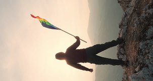 Silhouette Male Man Tourist Holding Gay Pride lgbt flag in Hands. Rainbow LGBTQ Flag on Top of Mountains - Lesbian, Gay, Bisexual, Transgender Social Movements. Vertical Video 4K slow motion