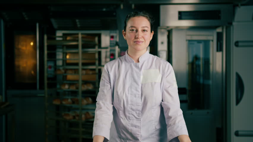 smiling beautiful woman baker in uniform stands near the oven before the start work bakery production of pastries Royalty-Free Stock Footage #1104765843