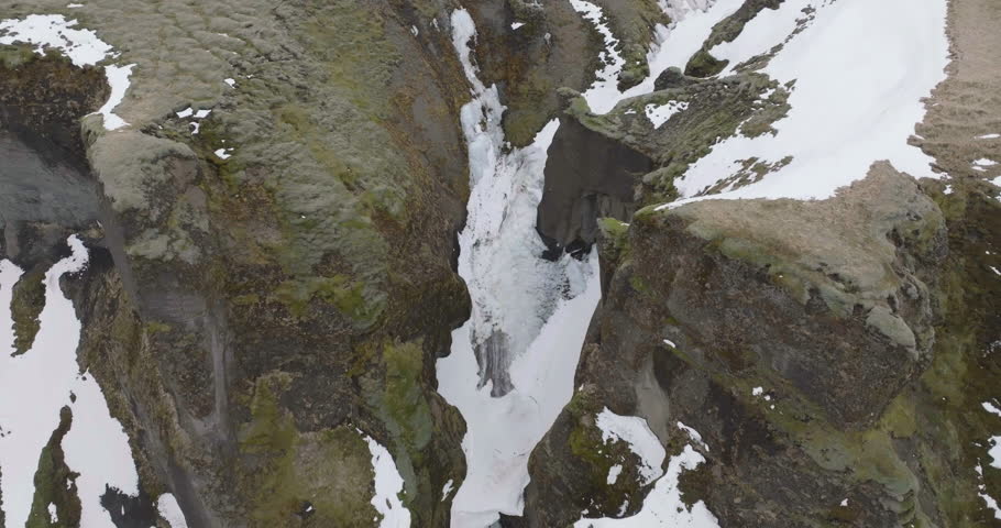 Aerial View of Almost Frozen Waterfall in Fjadrargljufur Canyon, Iceland, Volcanic Cliffs, Snow and Ice, Drone Shot