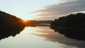 Amazing lake from above, aerial drone flies low over water surface during sunrise, beautiful island backlit with early morning sunlight. Rising sun and colored clouds in sky reflected in water mirror - Powered by Shutterstock - Get 15% off with code: PIKWIZARD15