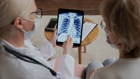 View from the back. The doctor shows the patient an X-ray of the chest on an electronic tablet. A young female doctor shows the results of the examination to an adult female patient. High quality 4k - Powered by Shutterstock - Get 15% off with code: PIKWIZARD15