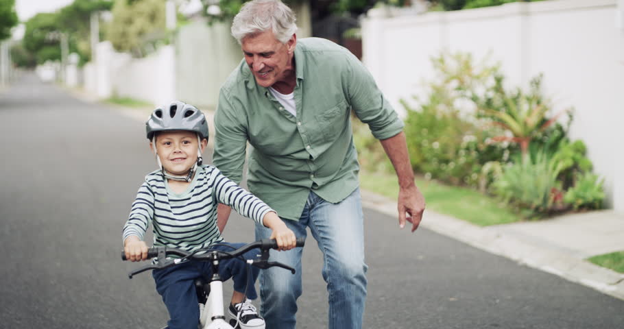 Happy, learning bike and a grandfather and child in the street for bonding, playing and childhood. Smile, family and an elderly man teaching a little boy kid to ride a bicycle with help in the road