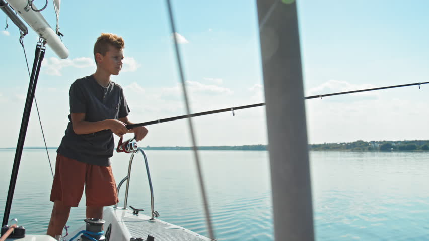 Caucasian boy wearing comfortable casual clothes fishing in lake using spinning rod during trip on yacht Royalty-Free Stock Footage #1104777521