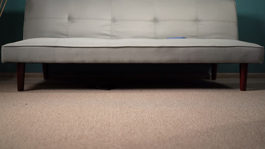 Handsome guy looking for a lost wallet under the sofa Royalty-Free Stock Footage #1104779743