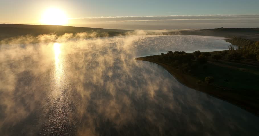Fog on a lake. Aerial drone view over sunset lake. Peaceful reflection of the beautiful sunset lake. Landscape during the evening, greenery