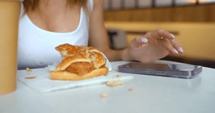 A young woman communicates online in a fast food cafe. Cropped video 4k. Junk food and social networks are the main harmful addictions of today's youth.