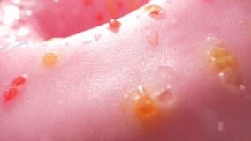 Immerse yourself in a stunning macro video featuring an array of captivating pink donuts. Each one is meticulously decorated with vibrant sprinkles and a luscious, glossy frosting. Dessert concept
