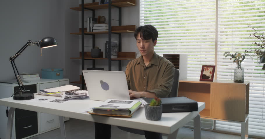 Efficient Asian Project Manager Working Diligently on a Laptop Computer in a Creative Agency Office, Skillfully Overseeing Successful Architectural Projects for a City Council Committee
