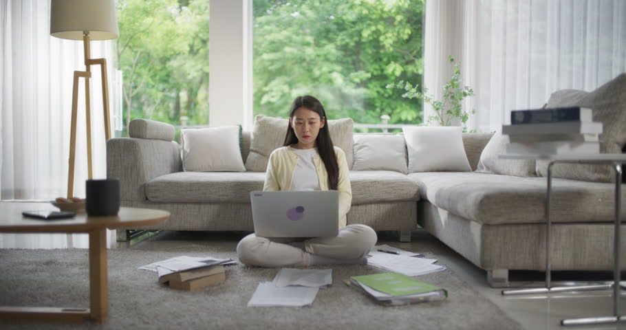 Young Beautiful Asian Female Browsing Internet, Using Laptop Computer at Home, Booking Places of Interest and Hotels for Her Vacation Trip While Sitting on a Floor in the Living Room Royalty-Free Stock Footage #1104788139